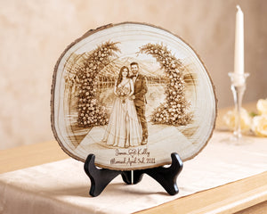 A personalized wooden slab plaque featuring a laser-engraved wedding portrait of a couple under floral arches, displayed on a black stand on a table runner with a candle in the background.