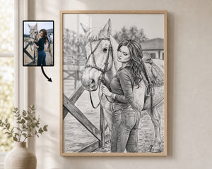 A framed black and white custom pencil sketch portrait of a woman and a horse, shown hanging on a beige wall next to a small inset photo of the reference image. The product is the framed art print itself.