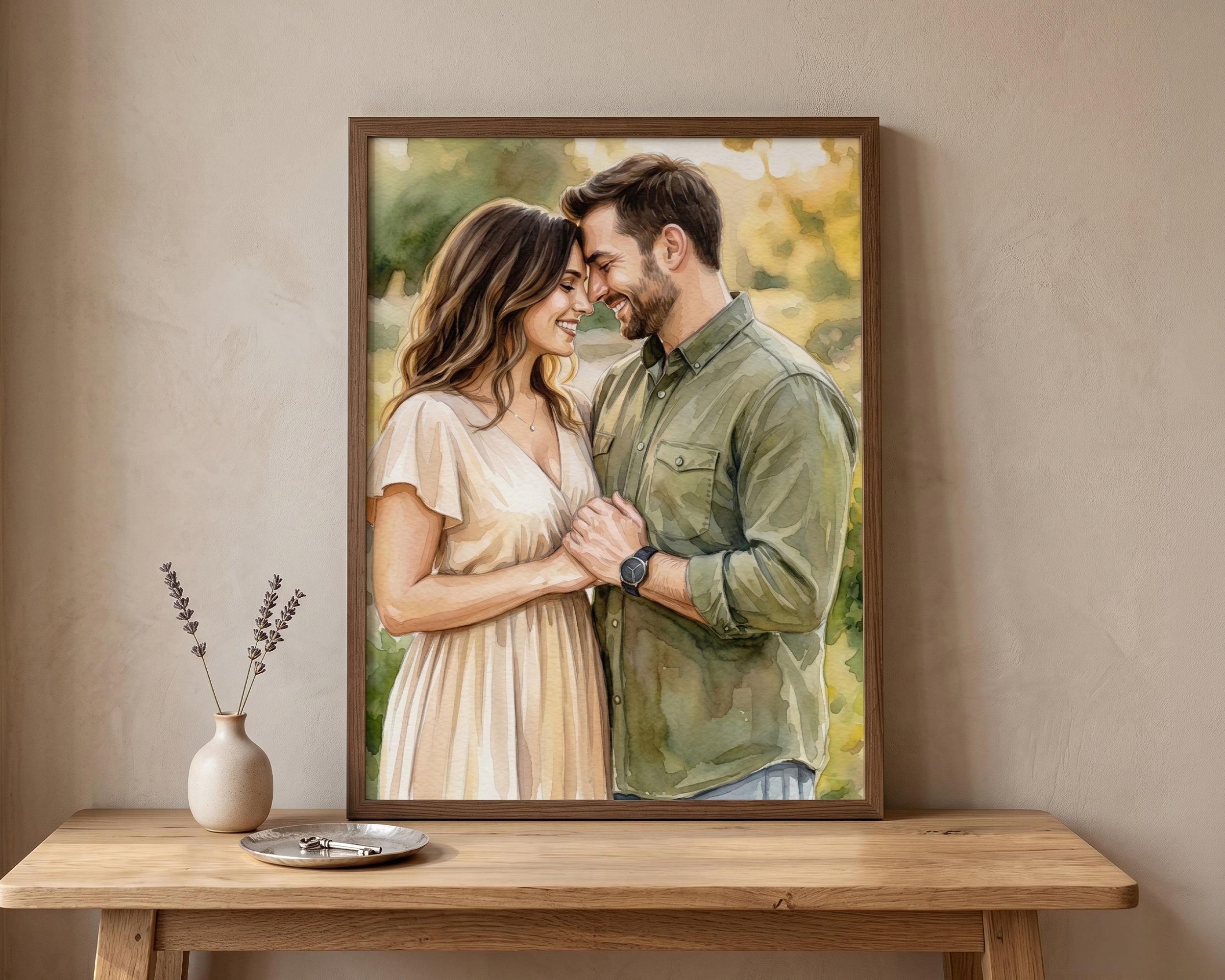 A framed custom watercolor portrait of a couple leaning in closely, displayed on a wooden console table against a textured beige wall with a small vase in the foreground.