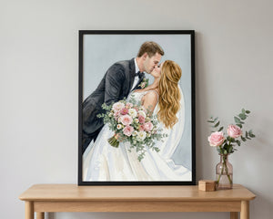 A framed custom wedding portrait print of a couple kissing, displayed on a light wood console table next to a vase of pink roses against a neutral gray wall.