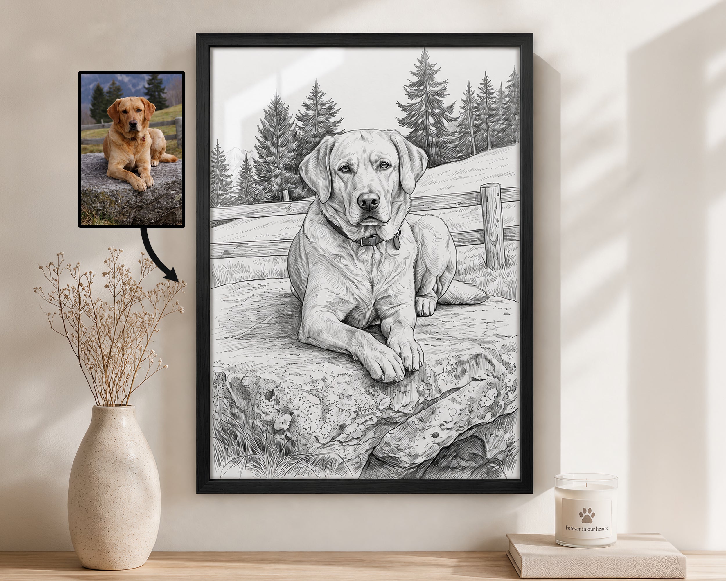 A framed black-and-white custom dog portrait of a Labrador Retriever is displayed on a wall in a styled room setting next to a vase with dried stems and a candle. A small inset photo of the reference dog lies to the left with an arrow pointing to the portrait.