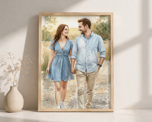A framed watercolor-style art print of a couple holding hands and walking outdoors, displayed leaning against a wall on a white surface next to a small vase with dried stems.