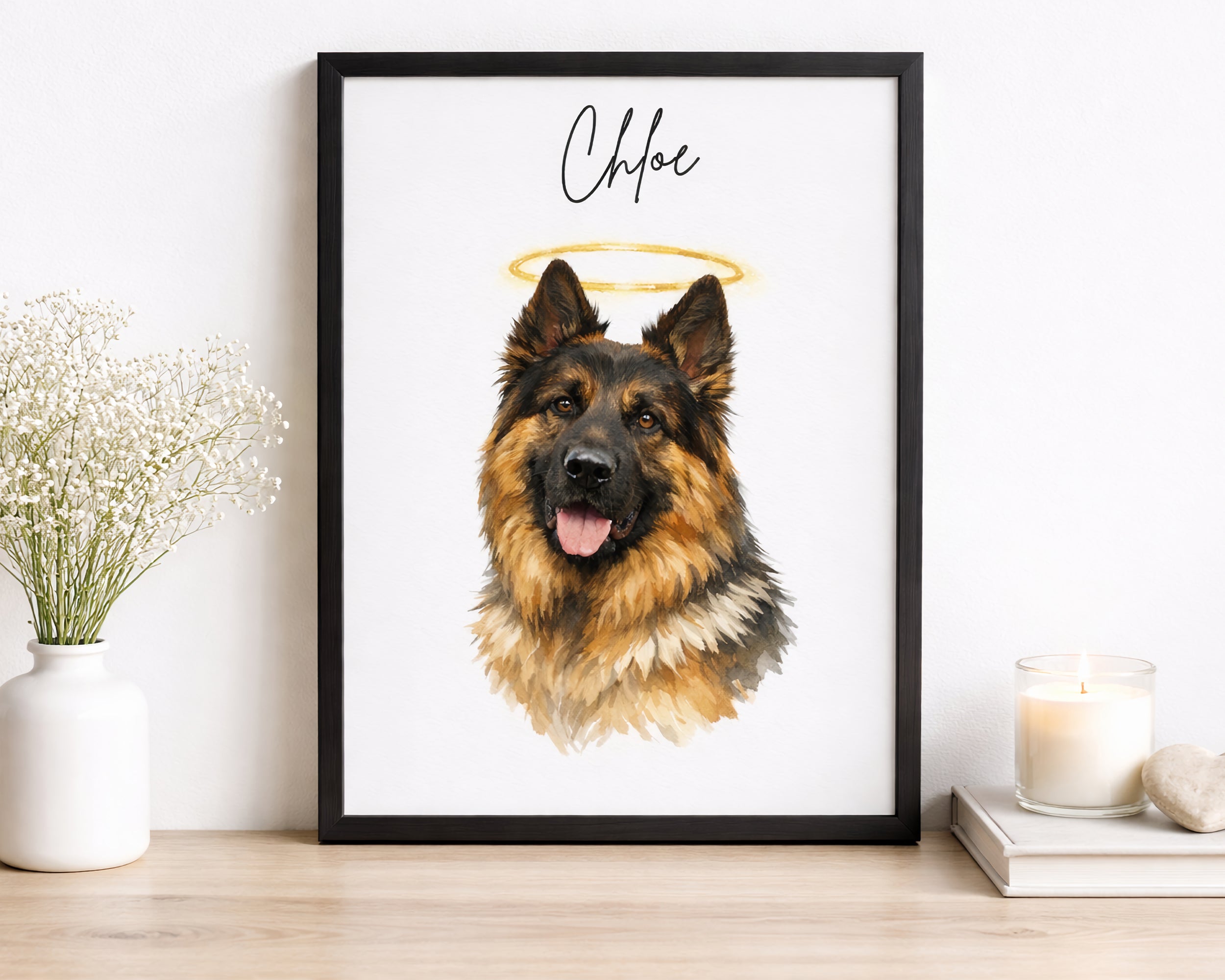 A framed custom pet portrait print featuring a German Shepherd dog with a gold halo and the name 'Chloe' in script, displayed on a wooden shelf next to a vase of baby's breath and a candle.