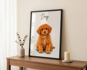 A framed custom pet portrait print featuring a fluffy orange puppy with the name 'Daisy' written in script, styled on a wooden console table with a vase and candle.