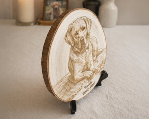 A round wooden plaque featuring a laser-engraved portrait of a dog with the text 'Mittsy 2012 - 2016', displayed on a small black stand on a light textured surface.