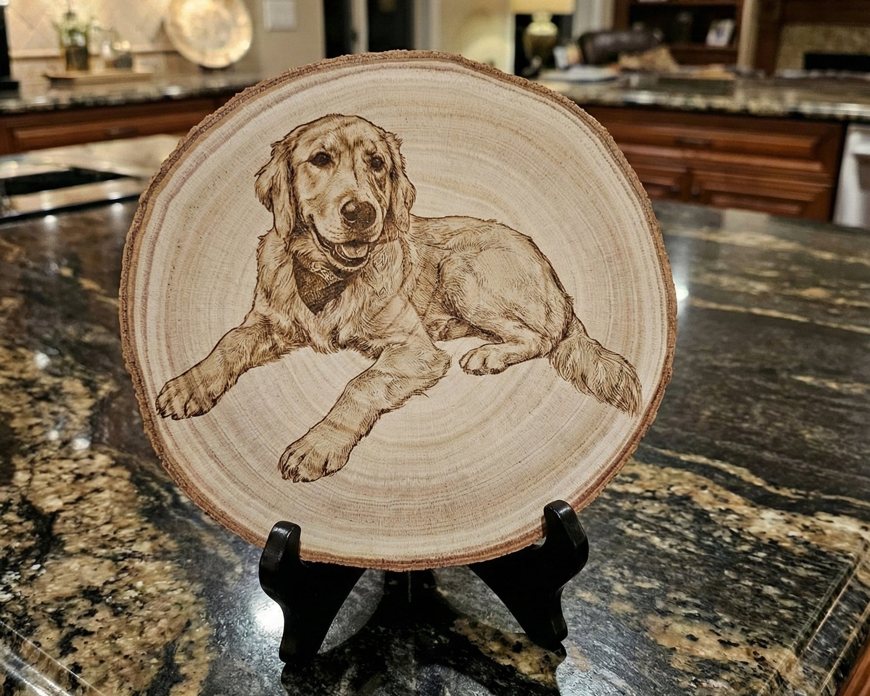 A round wood slice plate featuring a detailed brown engravving or pyrography illustration of a golden retriever dog, displayed on a small black stand on a kitchen countertop.