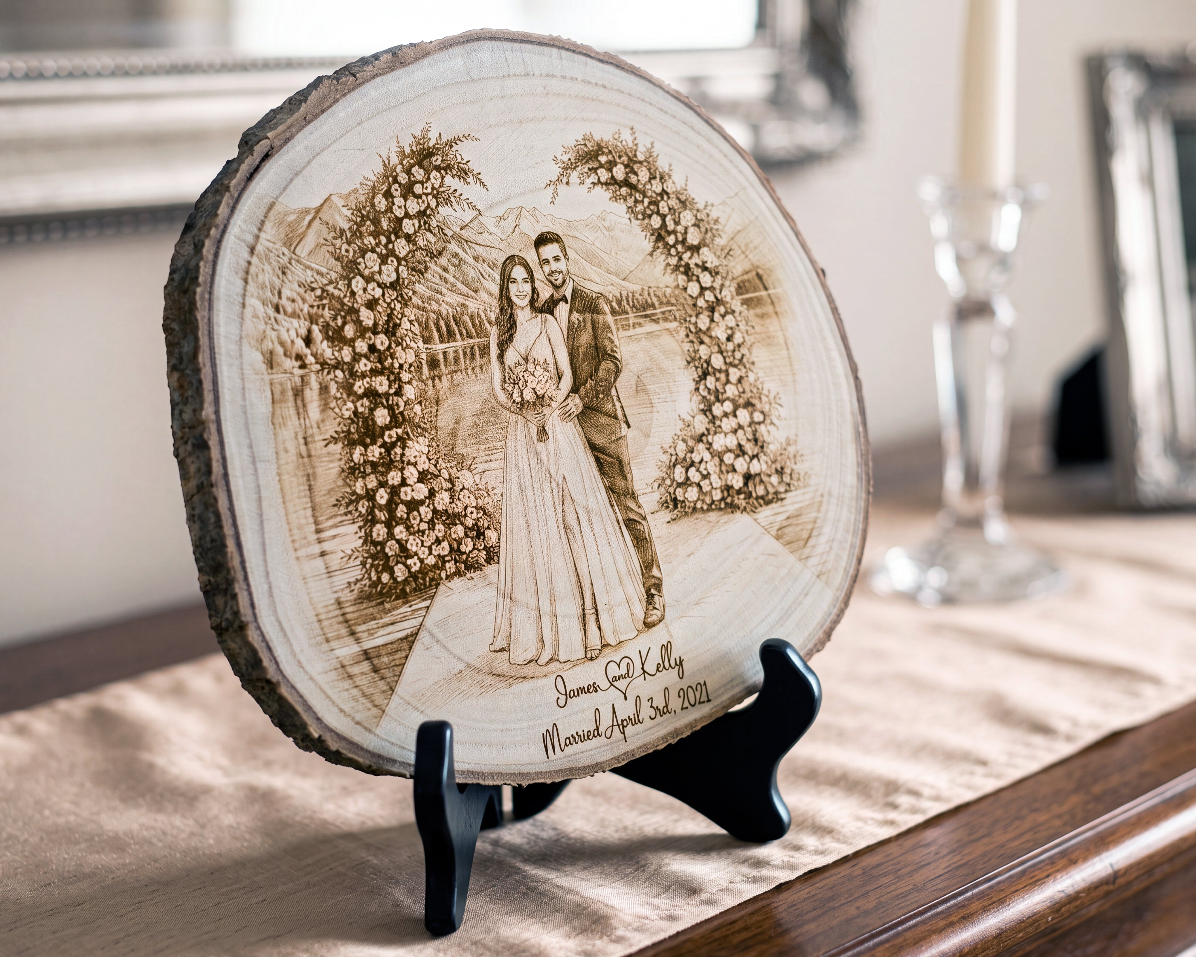 A round natural wood slice plaque with a laser-engraved wedding portrait of a couple under floral arches, displayed on a black stand on a table runner in a home setting.